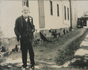 A suited man standing in a dirt path in front of a building