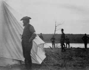 Black and white photo of a man standing beside a tent