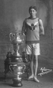 An athletic man stands beside a set of trophies