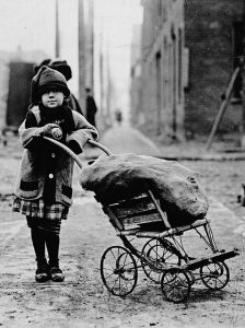 Black and white photo of a young girl wheeling a coal sack
