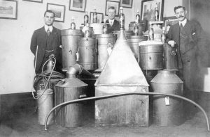 Three men stand around a collection of liquor stills