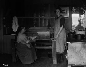 Two women standing at a weaving loom