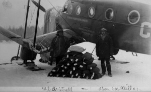 Two men outside of a small plane with a pile of cargo