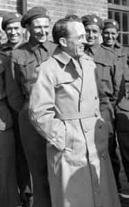 A smiling man stands in front of men in military garb