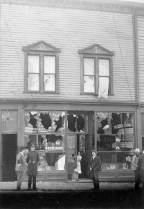 A police officer and others stand before a shop with broken windows