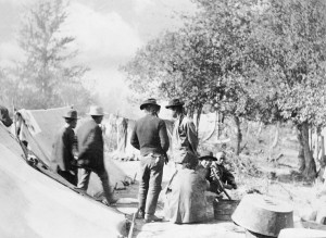 Men standing beside tents in a wooded camp