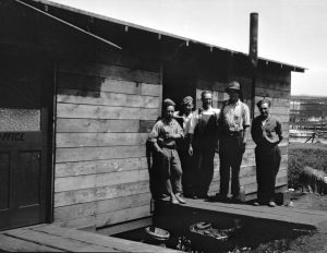 A group of men stand at the doorway of a small wooden building