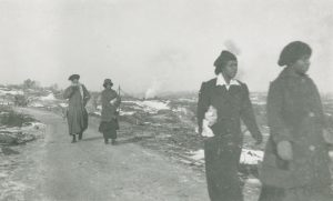 Four women walk a path lined with rubble