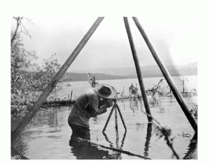 A man standing in a lake using a surveying tool