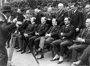 A group of well-dressed men sit and stand together before a photographer