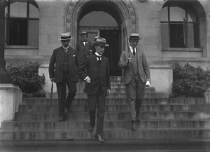 Three suited men descend a staircase