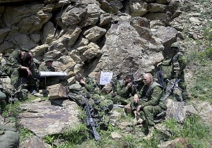 Men in military camo rest at the base of a rocky hill