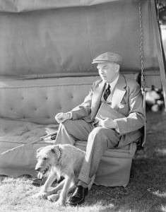 Mackenzie King sits on a couch, a dog at his feet