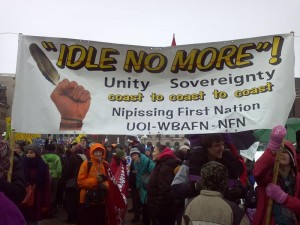 A crowd holds a sign reading "Idle No More! Unity Soveregnty coast to coast to coast"