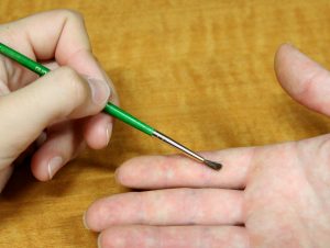 Clinician brushing the palmar surface of the right first finger with a small paintbrush