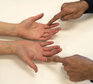 The patient is resting his hands close together on the table, palms up. The clinician is using their index fingers to stroke both the patient's index fingers at the same time