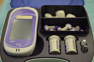 A blood glucose monitoring machine with cotton balls, lancets, and reagent strips