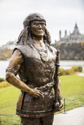 Statue of Tessouat, Algonquin Chief who controlled trade along the Ottawa River in the first half of the 17th century and who denied Champlain passage further west. Parliament buildings in the background. Credits to: Canadian Heritage