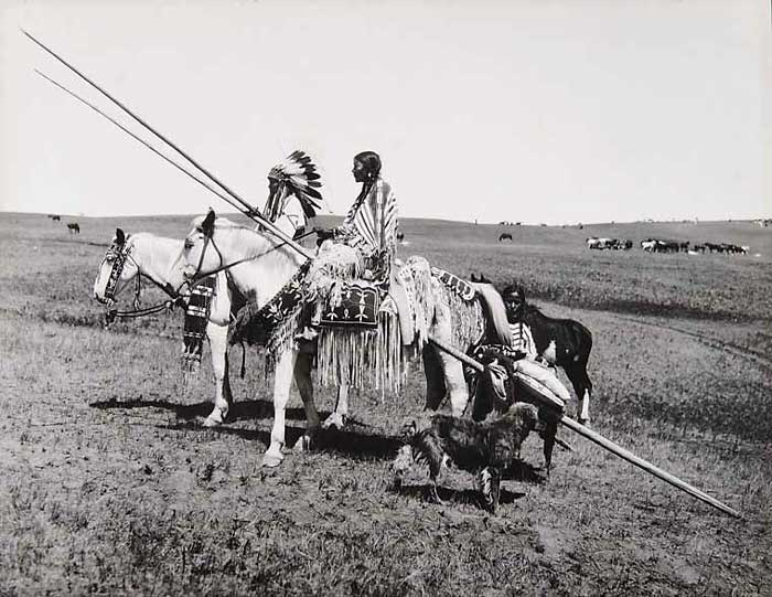 Photo of  Sioux family. The woman appears to be doing the heavy lifting while the man is just riding his horse.