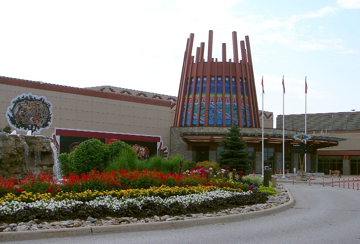 This photo shows the entrance to Casino Rama, which is a large, low, rectangular building with a glamourous, somewhat tipi-shaped entrance. There are 3 flagpoles out in front, but we can't make out which flags they are. There is a beautiful section of landscaped garden in front of the building.