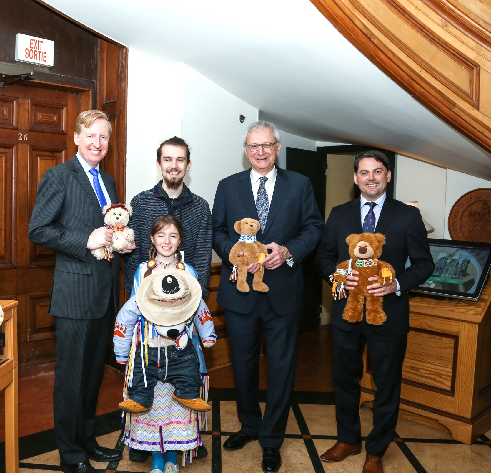 May 10th is Bear Witness Day, an important day in the history of Jordan’s Principle. Plush bears are being held as symbols (Premier Blaine Higgs, Minister Jake Stewart and Minister Dominic Cardy with invited guests Candra Perley and Cole Perley). Credits to: Province of New Brunswick.
