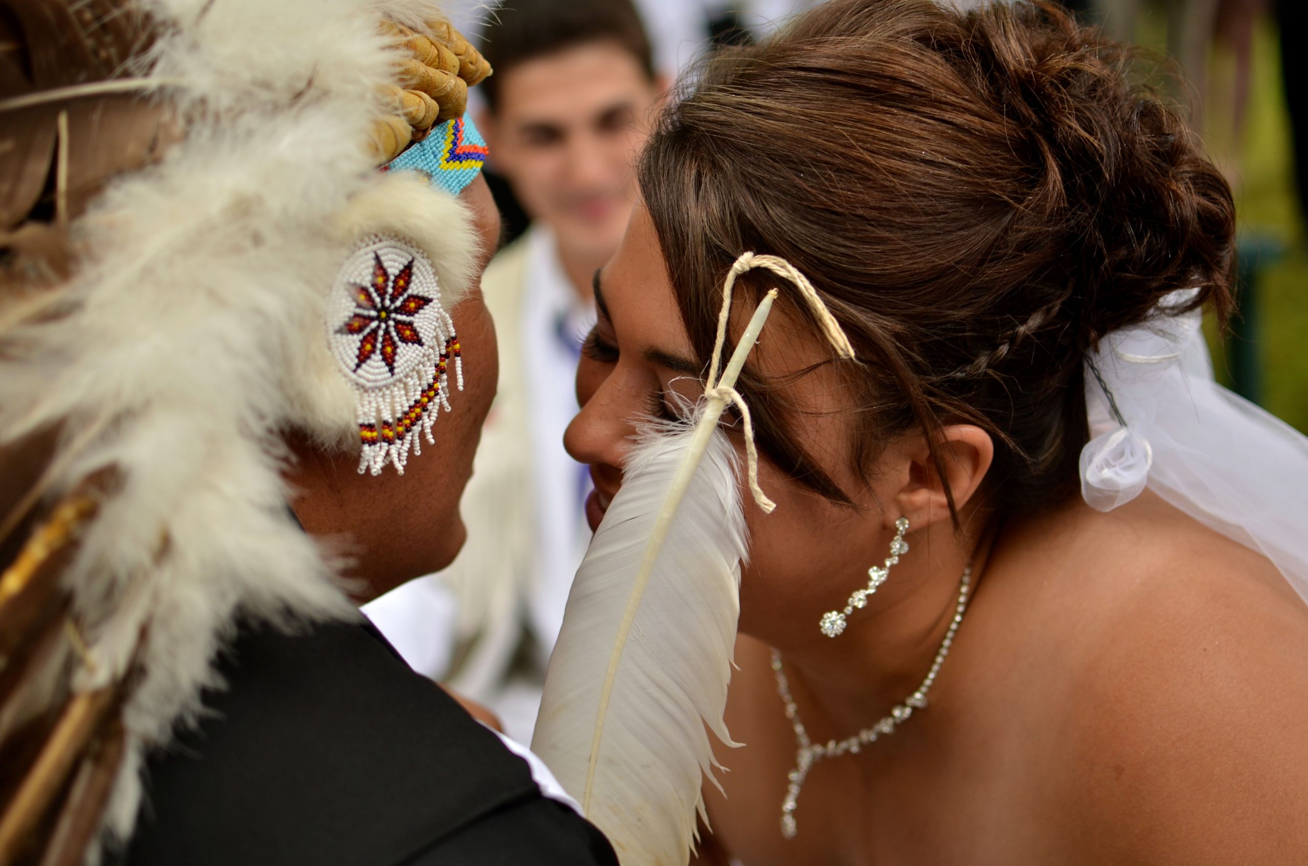 The photo appears to show a Mi'kmaw bride being blessed by a male elder who is wearing a headdress and holding a white feather.