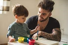 a father sitting beside his child who is painting