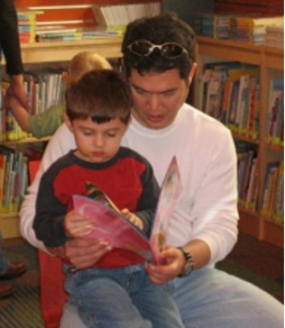 image of son sitting on father's lap reading a book together