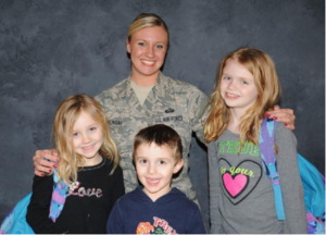 Photo of a mother in army uniform with arms around her 3 young children.