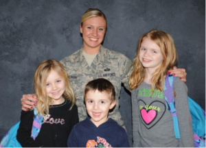 Photo of a mother in army uniform with arms around her 3 young children. 