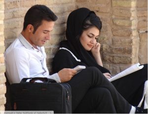 Two young adults sitting against a brick wall, reading.