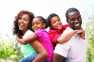 Two smiling parents (male & female) each holding a holding a child on their back. 