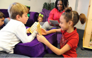 Photo of 3 children in the living room with a mother sitting and reading. 