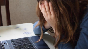 Young girl with her face in her hands, bent over a laptop.