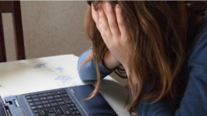 Young girl with her face in her hands, bent over a laptop. 