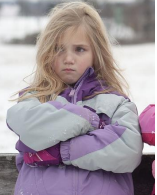 Picture or blond child in ski jacket, arms crossed in front of her and pout on her face.