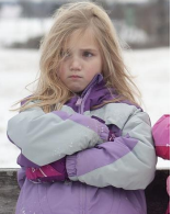 Picture or blond child in ski jacket, arms crossed in front of her and pout on her face. 