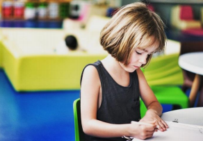 Picture of female child with blond bob sitting at a desk writing in a notebook.