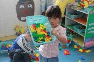 Child holding up a bin of coloured plastic numbers.