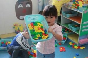 Child holding up a bin of coloured plastic numbers. 