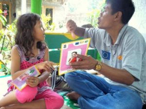 Photo of adult male holding up a flashcard for a young child.