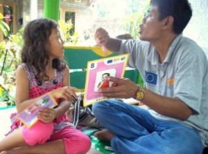 Photo of adult male holding up a flashcard for a young child. 