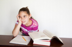 Child with one hand on the side of her face as she sits in front of as a stack of books.
