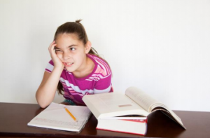 Child with one hand on the side of her face as she sits in front of as a stack of books. 