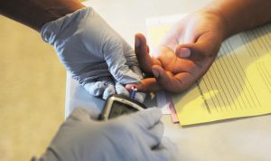 An adult doing a finger prick test on a child's middle finger 