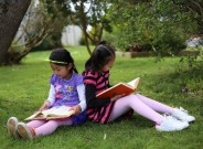 Two children sitting on the grass reading books