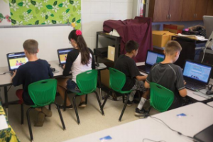 Image of 4 children sitting at computers in a classroom.