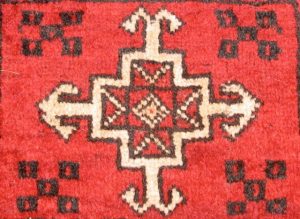 Figure 1-2 shows a red woven rug with patterns in black and white. At the center of the rug is a diamond, which is encased in a square. The square sits centrally in a larger cross/plus sign. An arrow-like form extends from the end of each arm of the cross.