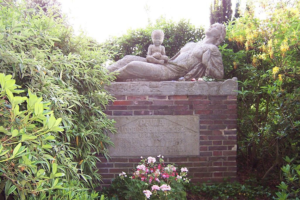 Figure 1-9. A photograph of Paula Modersohn-Becker's gravesite. The monument is made of brick at the base, but a sculpted stone figure of a woman lays across the top, breasts exposed, and looking upward. A baby sits cross-legged on top of her hips.