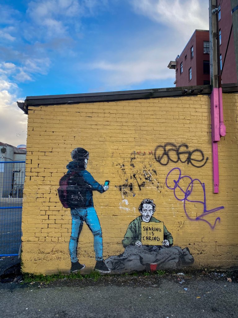 man in black jacket and blue denim jeans standing beside yellow wall with graffiti during daytime photo